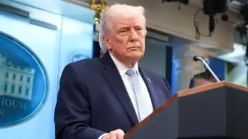 Donald Trump speaks at a podium with flags in the background.