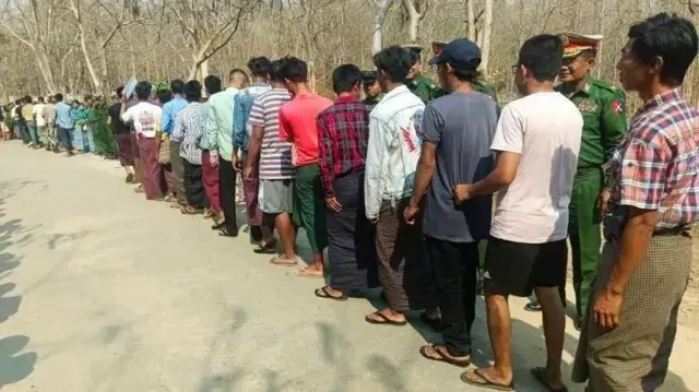 رجال يقفون على جانب طريق تحت مراقبة جنود